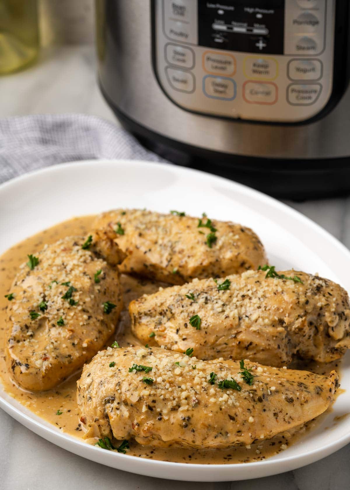 tender instant pot chicken breast with a pan sauce on a plate with instant pot in background