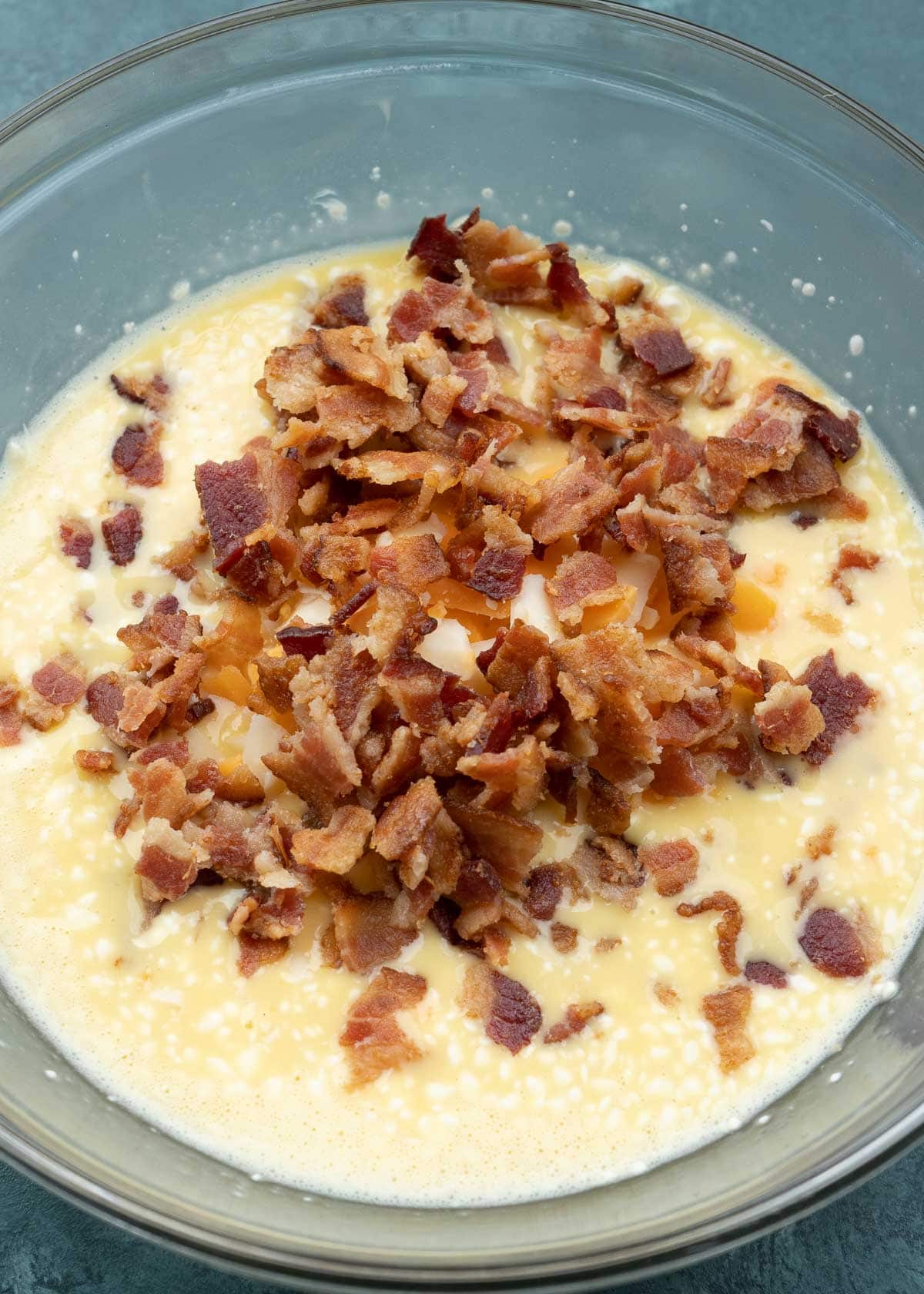 eggs, cream cheese, shredded cheese, and bacon in a glass bowl