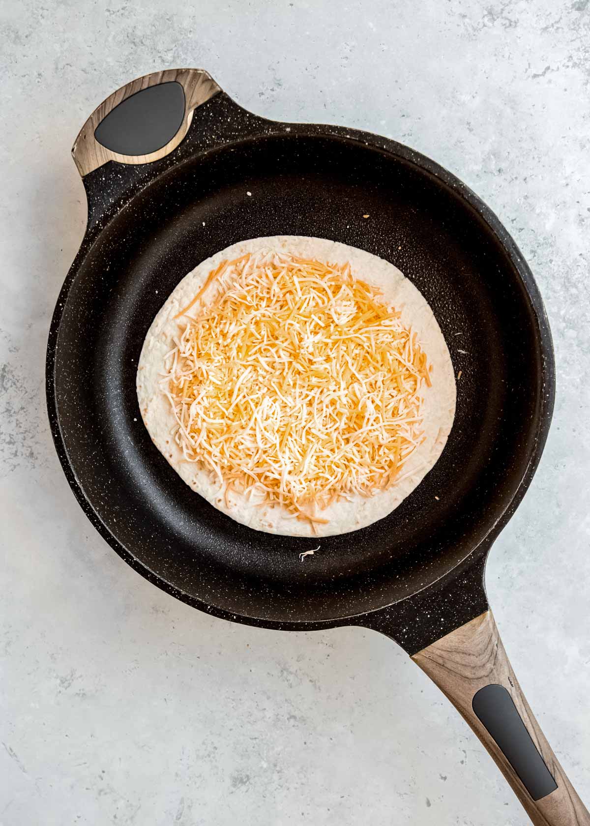 tortilla with shredded cheese in skillet