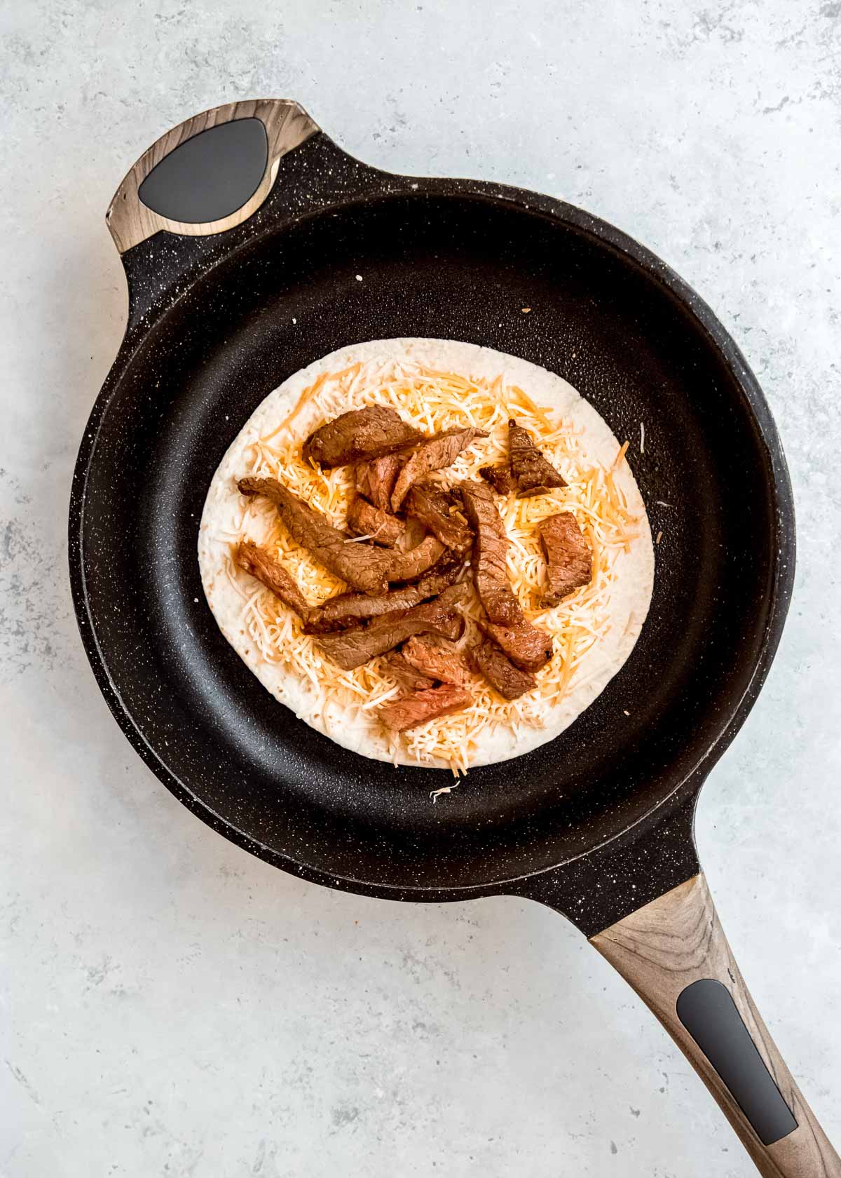 steak and shredded cheese in skillet