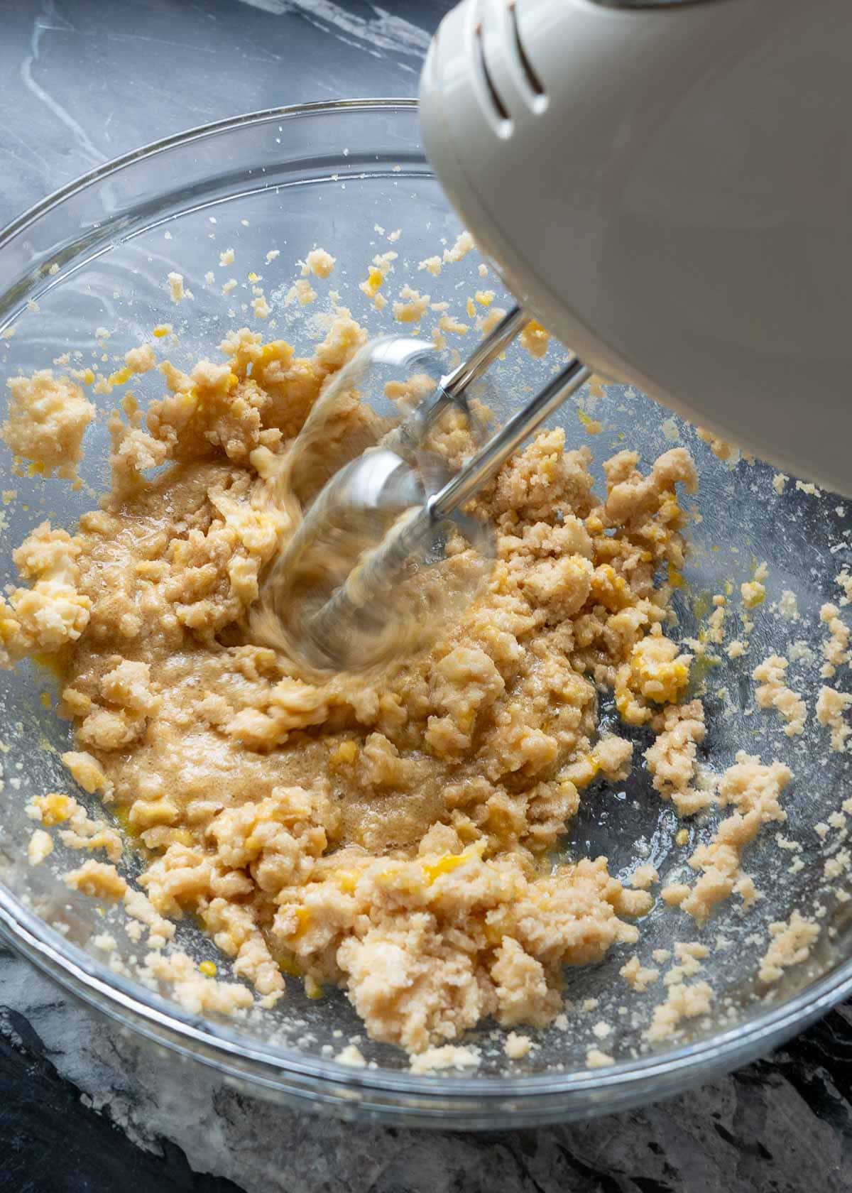 electric mixer beater mixing the egg into the brown sugar and butter in a glass bowl
