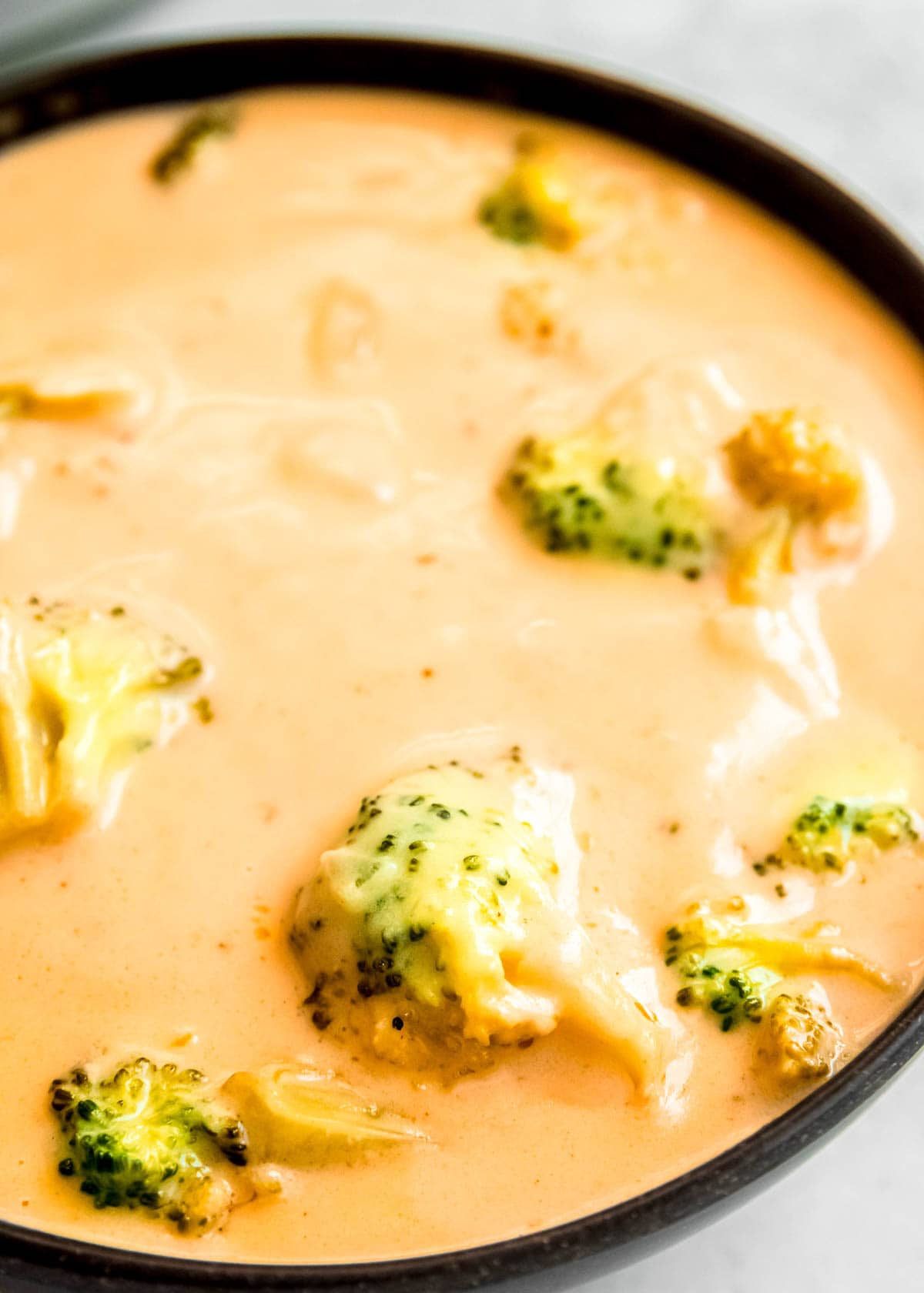 closeup shot of broccoli cheddar soup in a black rimmed bowl