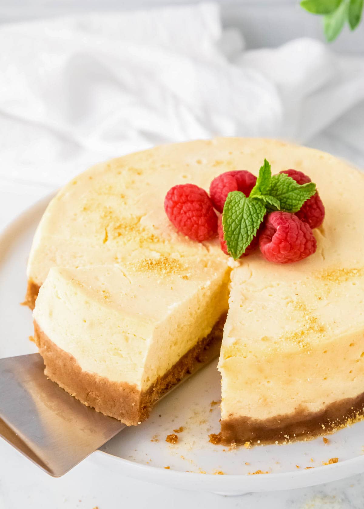 cutting a slice of instant pot cheesecake with raspberries on top