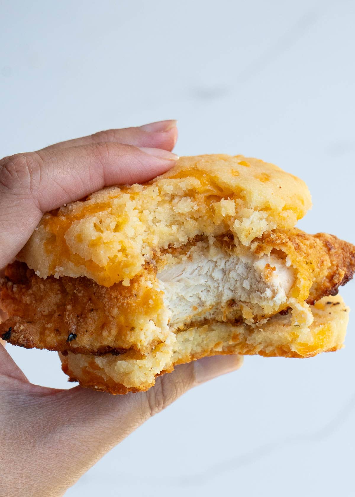 a photo of someone holding a chicken and biscuit with a bite taken out of it.