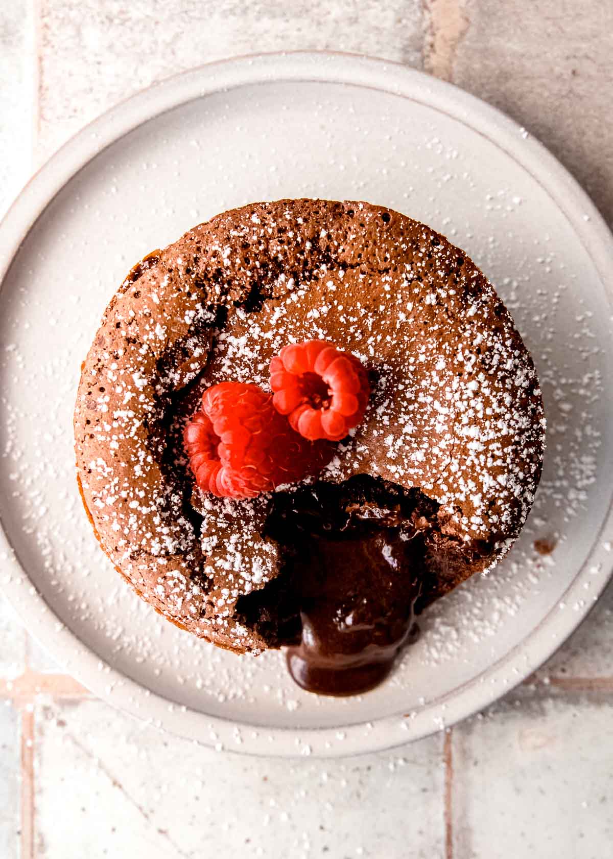 overhead shot of gluten free molten lava cake topped with two raspberries on a white plate