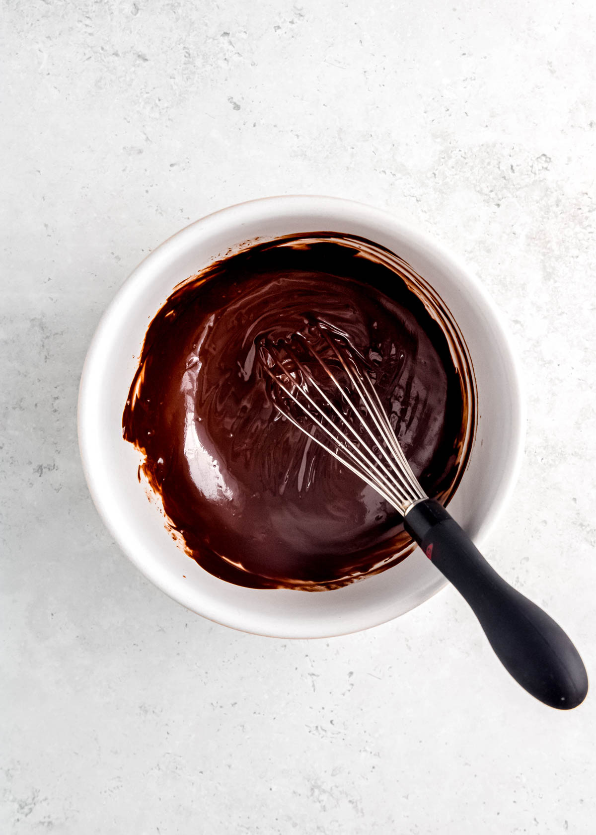 melted chocolate and butter mixed with a whisk in a white bowl