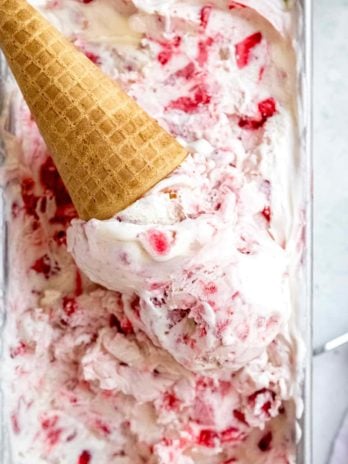 no churn strawberry ice cream scooped into a waffle cone on top of the batch of homemade ice cream