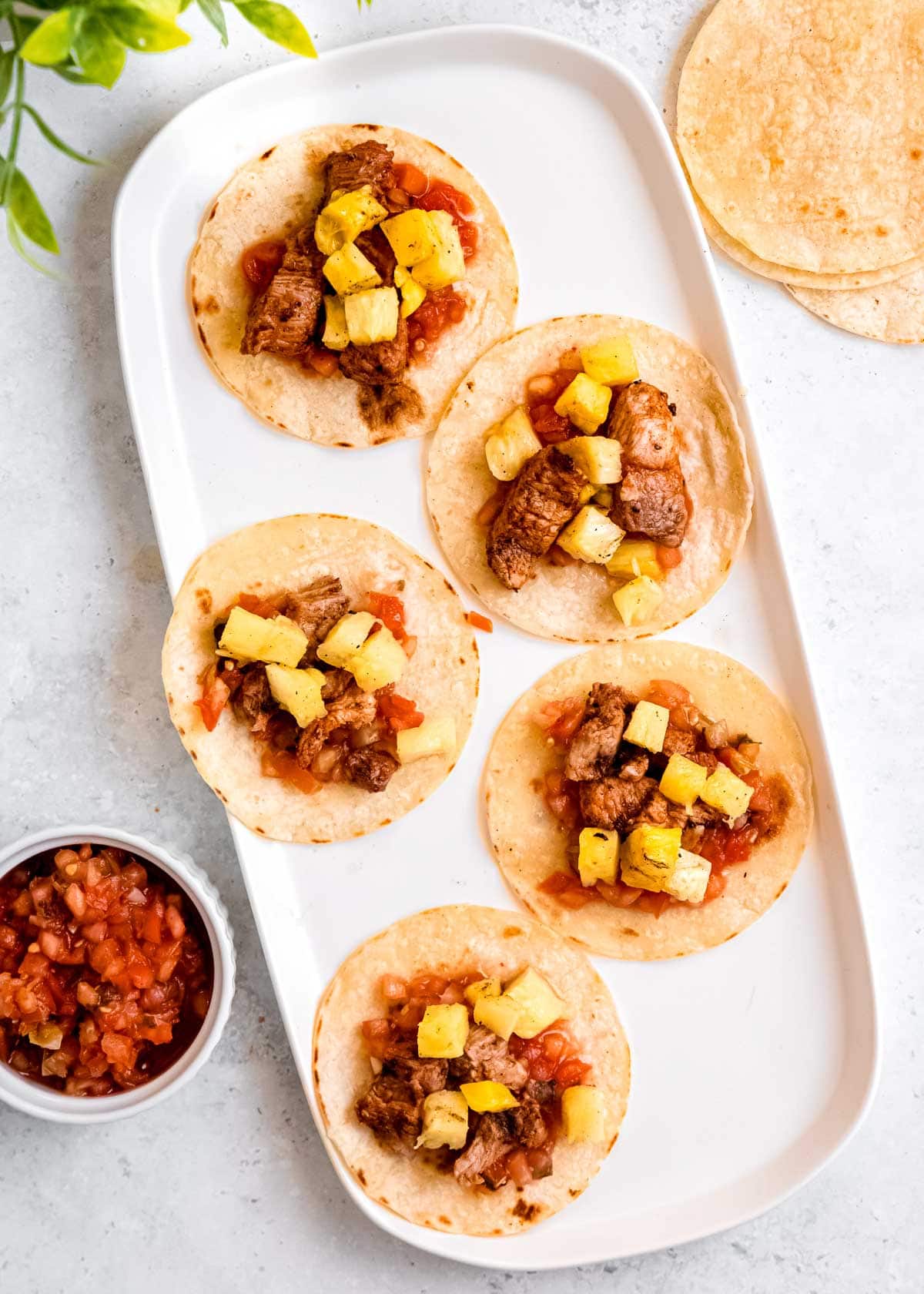 tacos al pastor being assembled on white platter