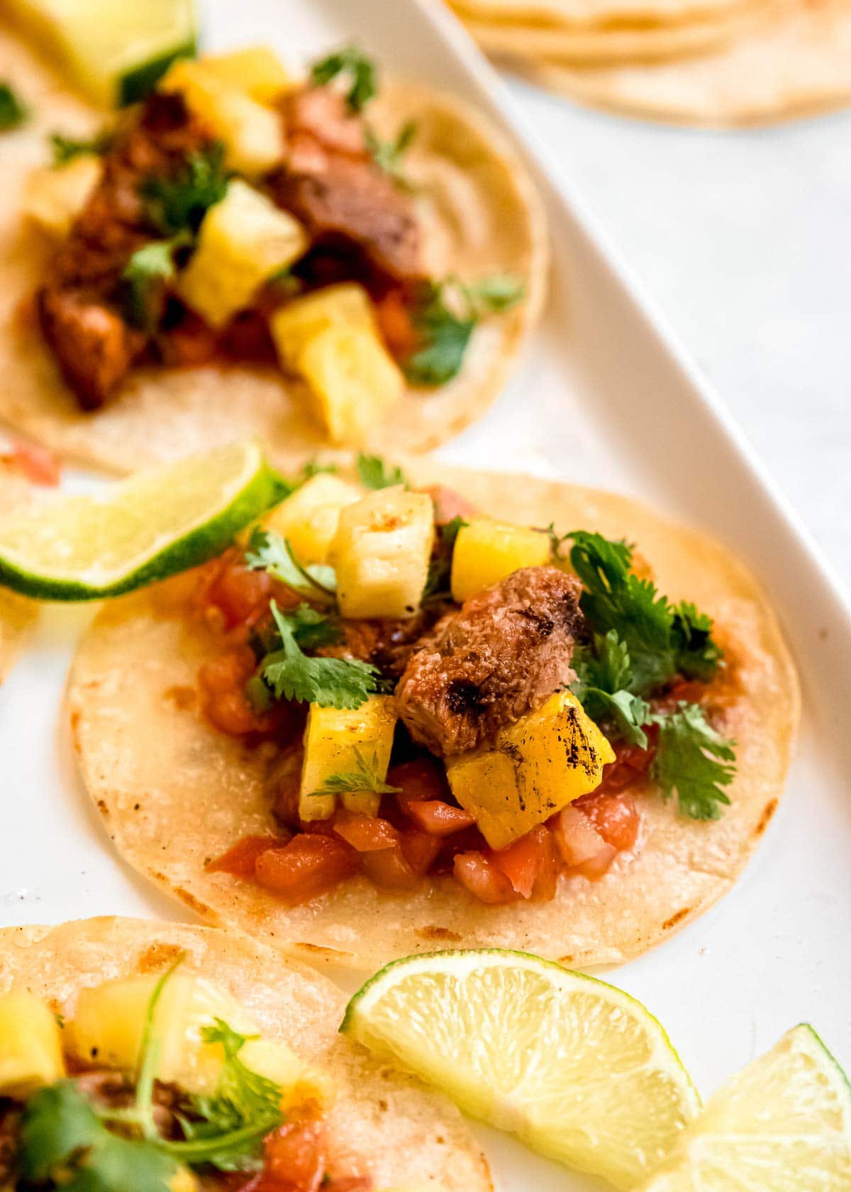 close up of tacos al pastor on white platter