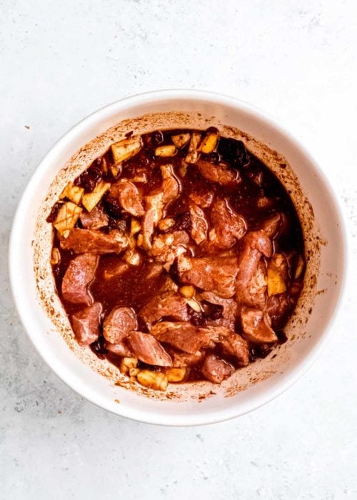 sliced pork shoulder being added to marinade in white bowl