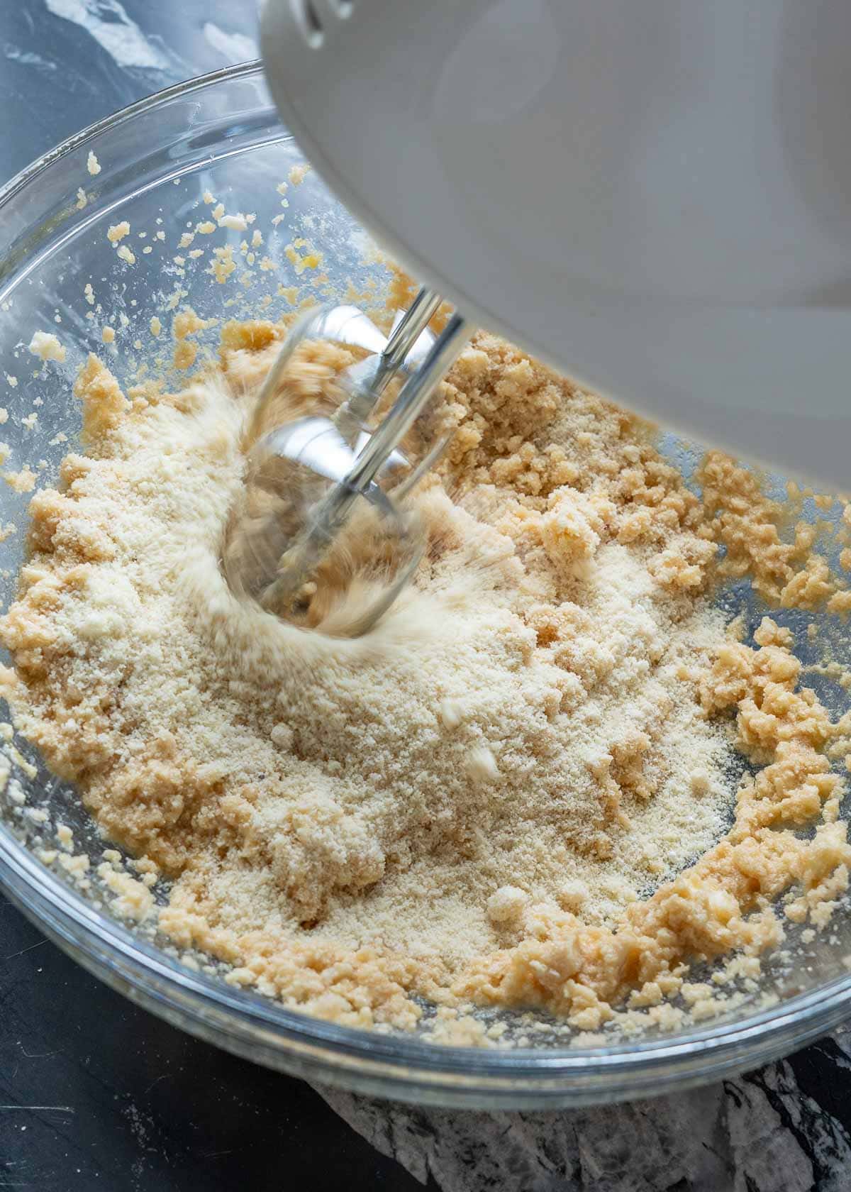 almond flour, baking soda, baking powder, and salt being beaten into the wet keto cookie dough ingredients