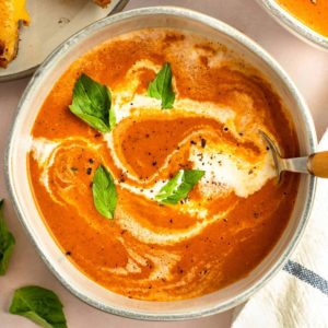 tomato soup in a bowl with a drizzle of heavy cream and basil