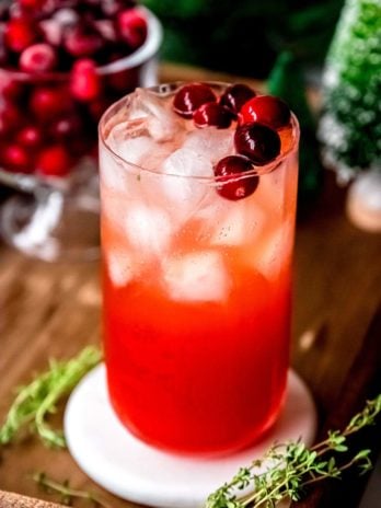 cranberry spritz in a tall glass with ice and cranberry garnish