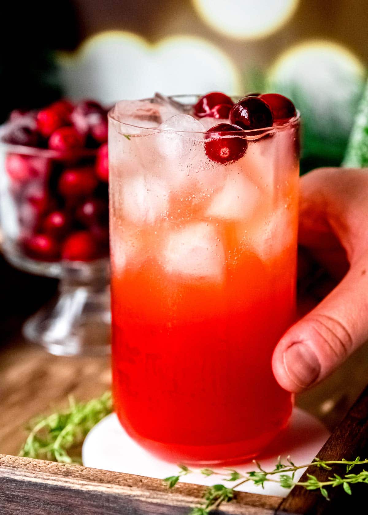 hand grabbing a cranberry spritz garnished with cranberries and thyme