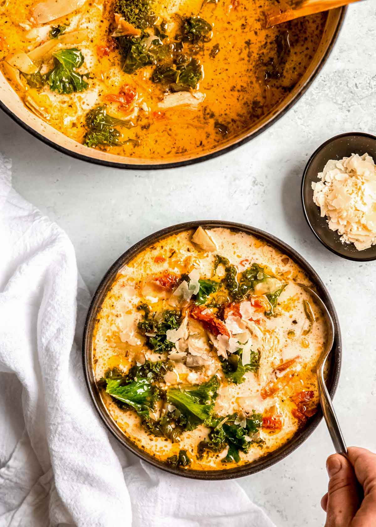 an overhead shot of tuscan chicken soup in a pit and in a black bowl with a spoon