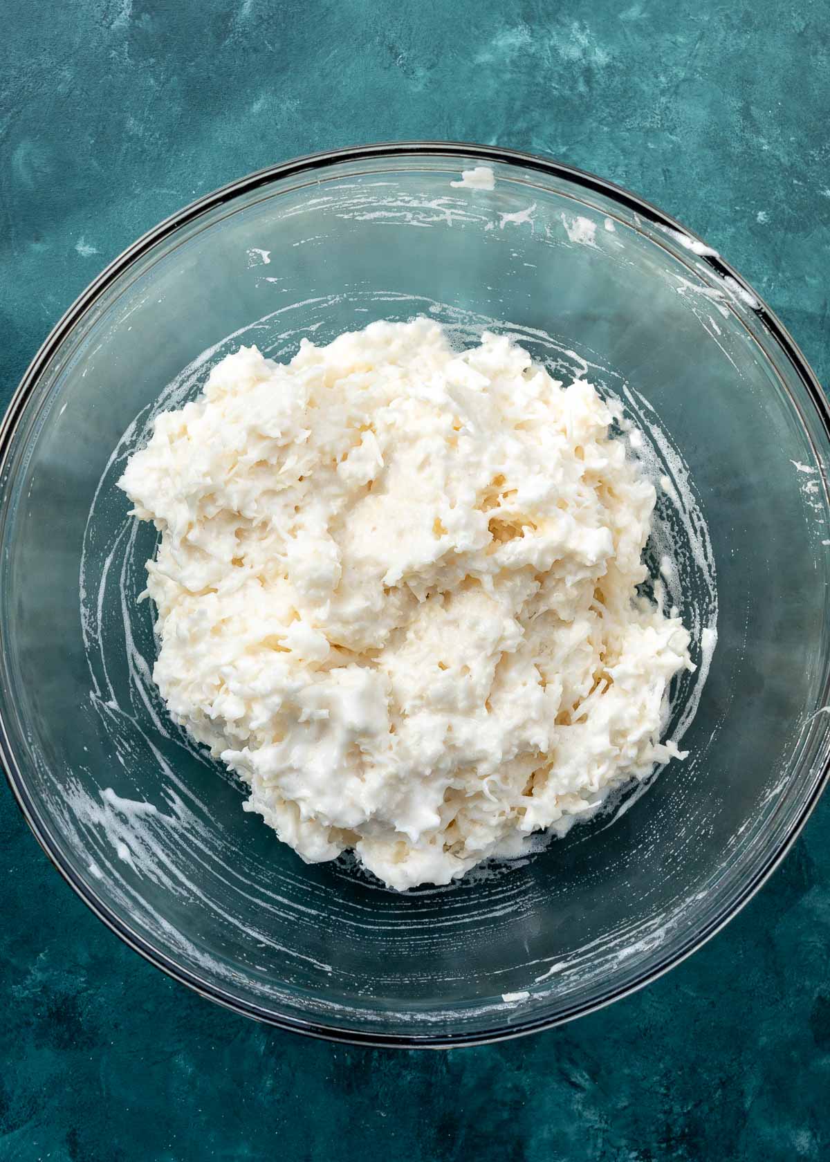 overhead shot of coconut being added to macaroons in clear mixing bowl