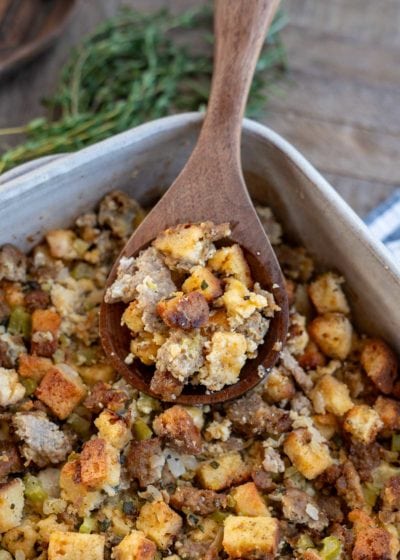 an overhead shot of sausage stuffing in a dish with a brown spoon and herbs on the side.