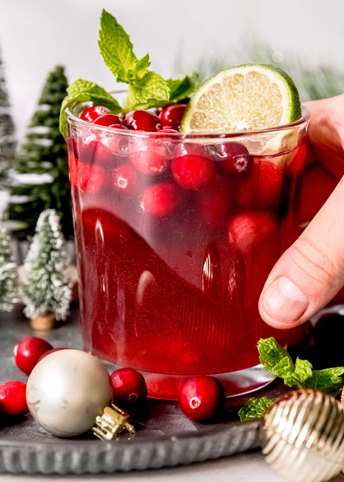 a hand picking up a glass full of the best holiday cocktail, Christmas Punch (with champagne, cranberries, and pomegranate)
