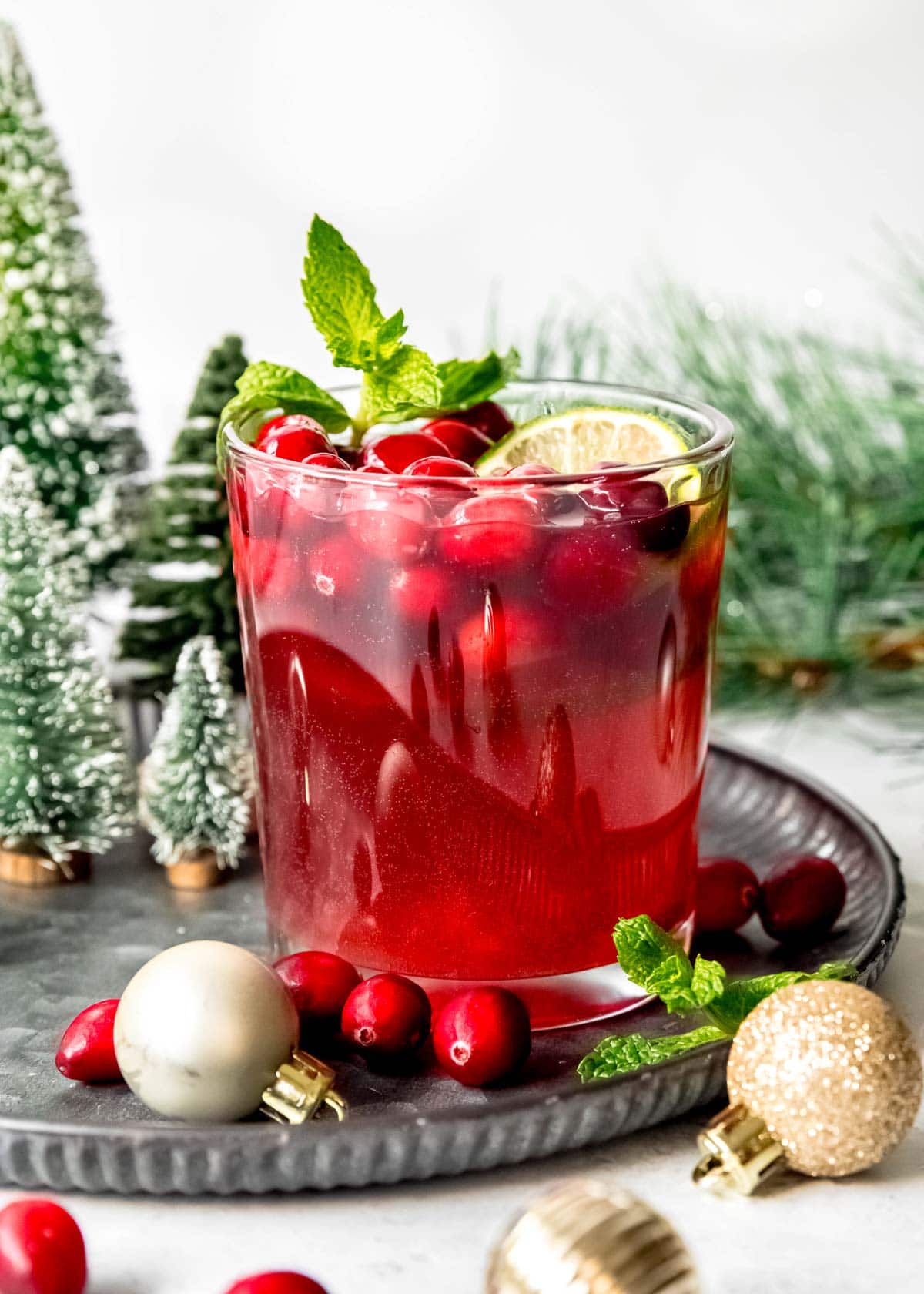 a glass of christmas punch sitting on a tray with holiday items