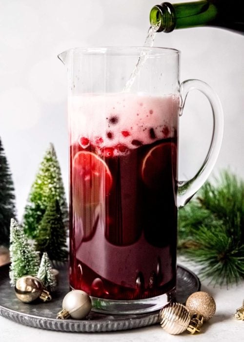 Champagne being poured into holiday punch. This christmas cocktail includes cranberries, limes, pomegranate juice, and cointreau for a citrus flavor.