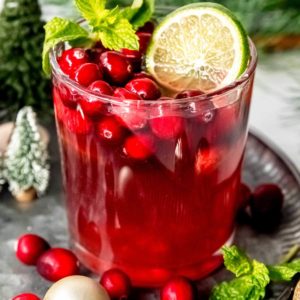 a glass full of christmas punch, cranberries, lime slices, and mint leaves