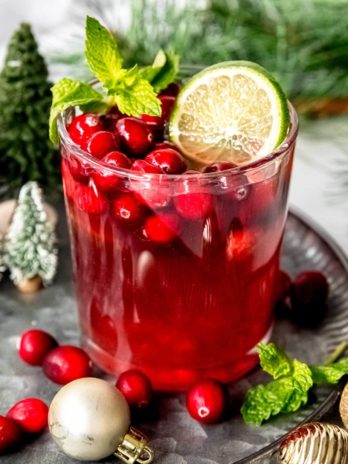 a glass full of christmas punch, cranberries, lime slices, and mint leaves