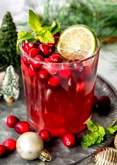 a glass full of christmas punch, cranberries, lime slices, and mint leaves