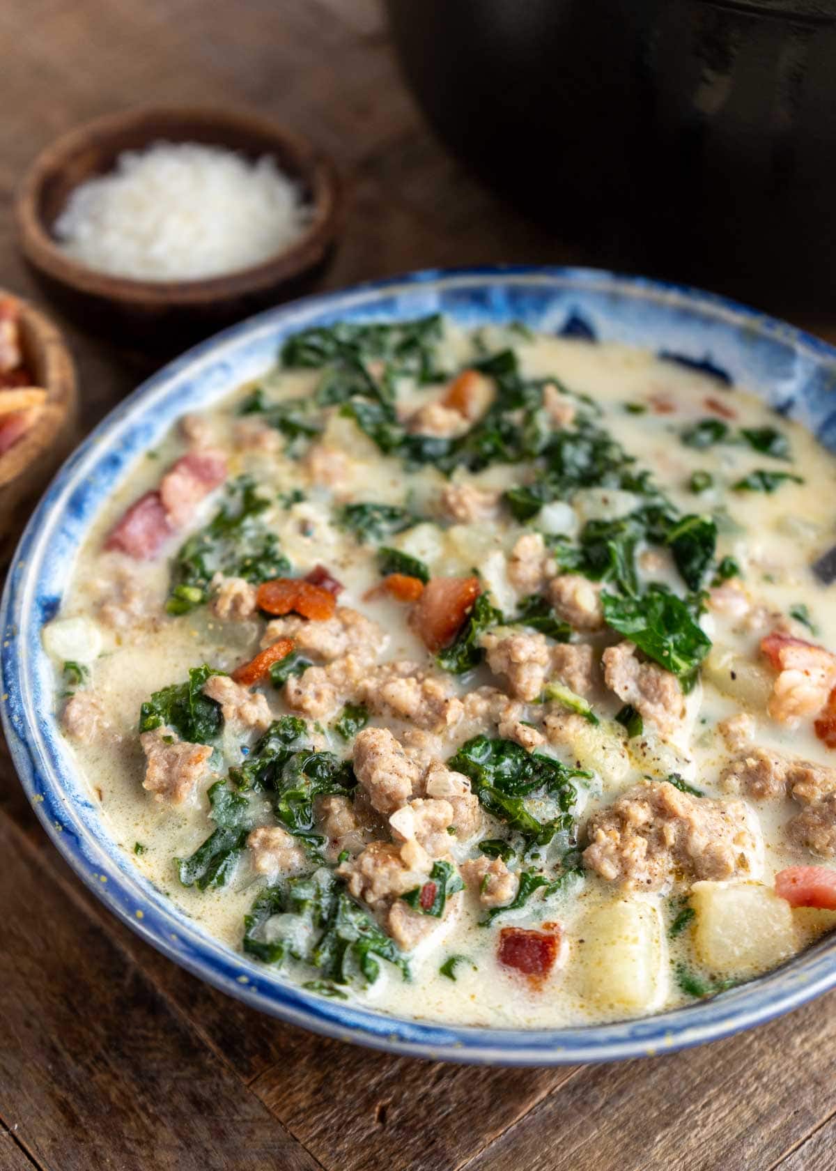 a bowl of zuppa toscana with parmesan and extra bacon on the side