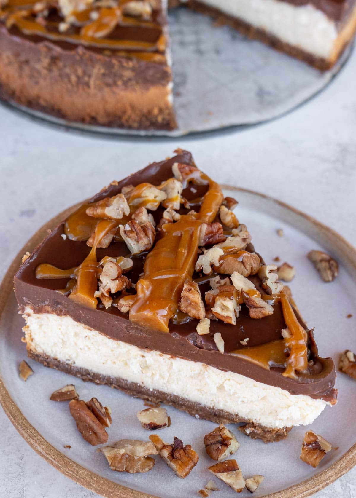 a slice of turtle cheesecake on a plate with roasted pecans