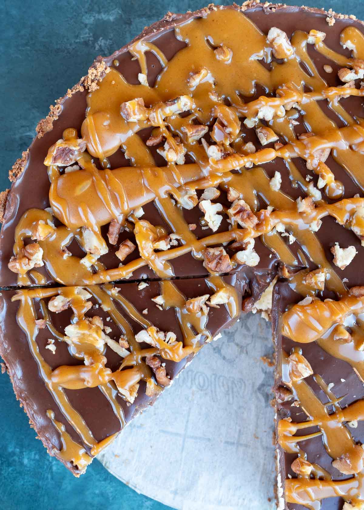 a close up shot of cheesecake with chocolate, caramel and pecans with one slice missing