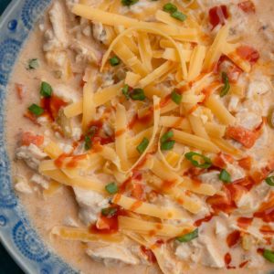 an overhead shot of buffalo chicken soup with shredded cheddar and green onions on top.