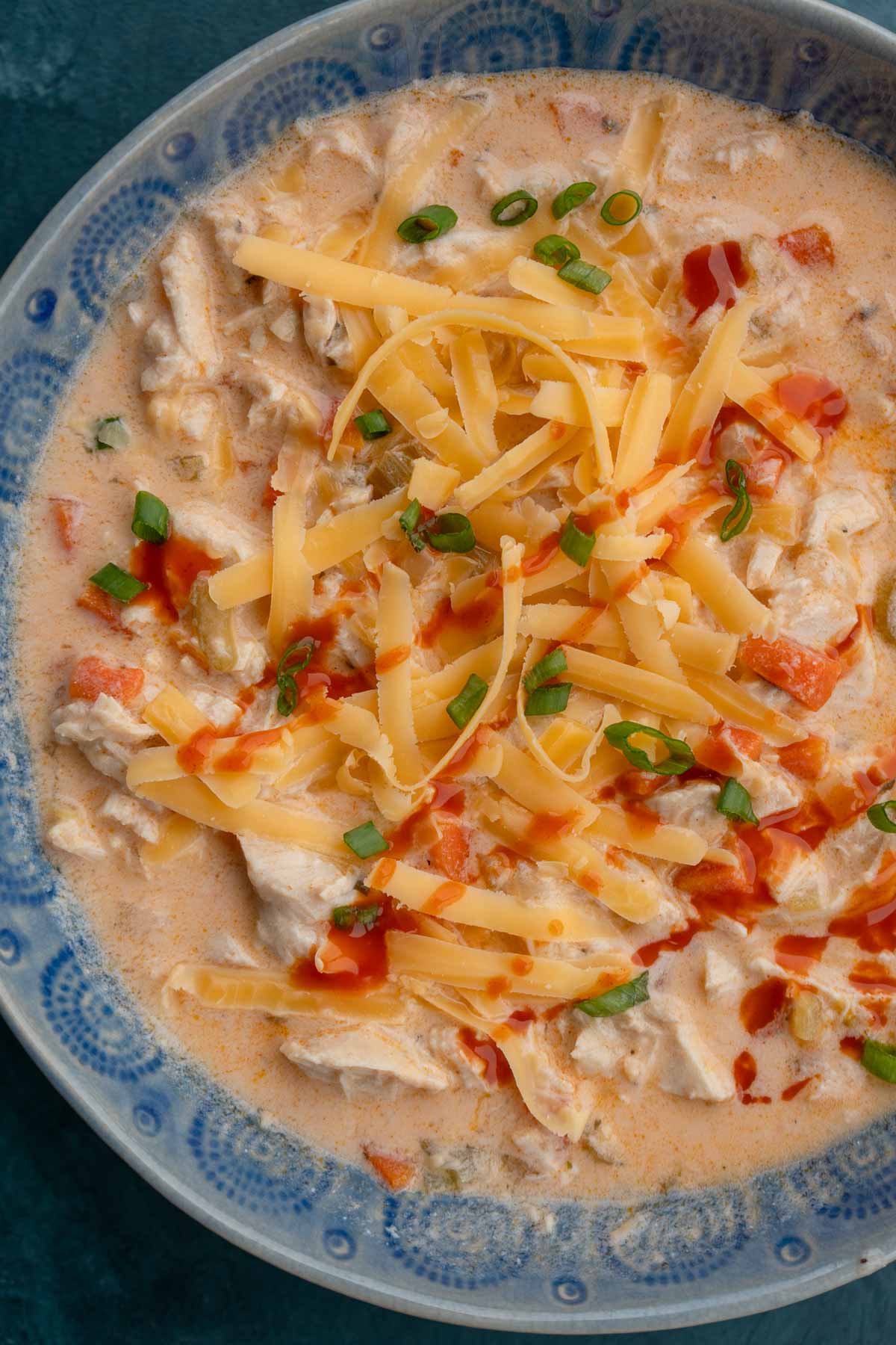 an overhead shot of buffalo chicken soup with shredded cheddar and green onions on top.