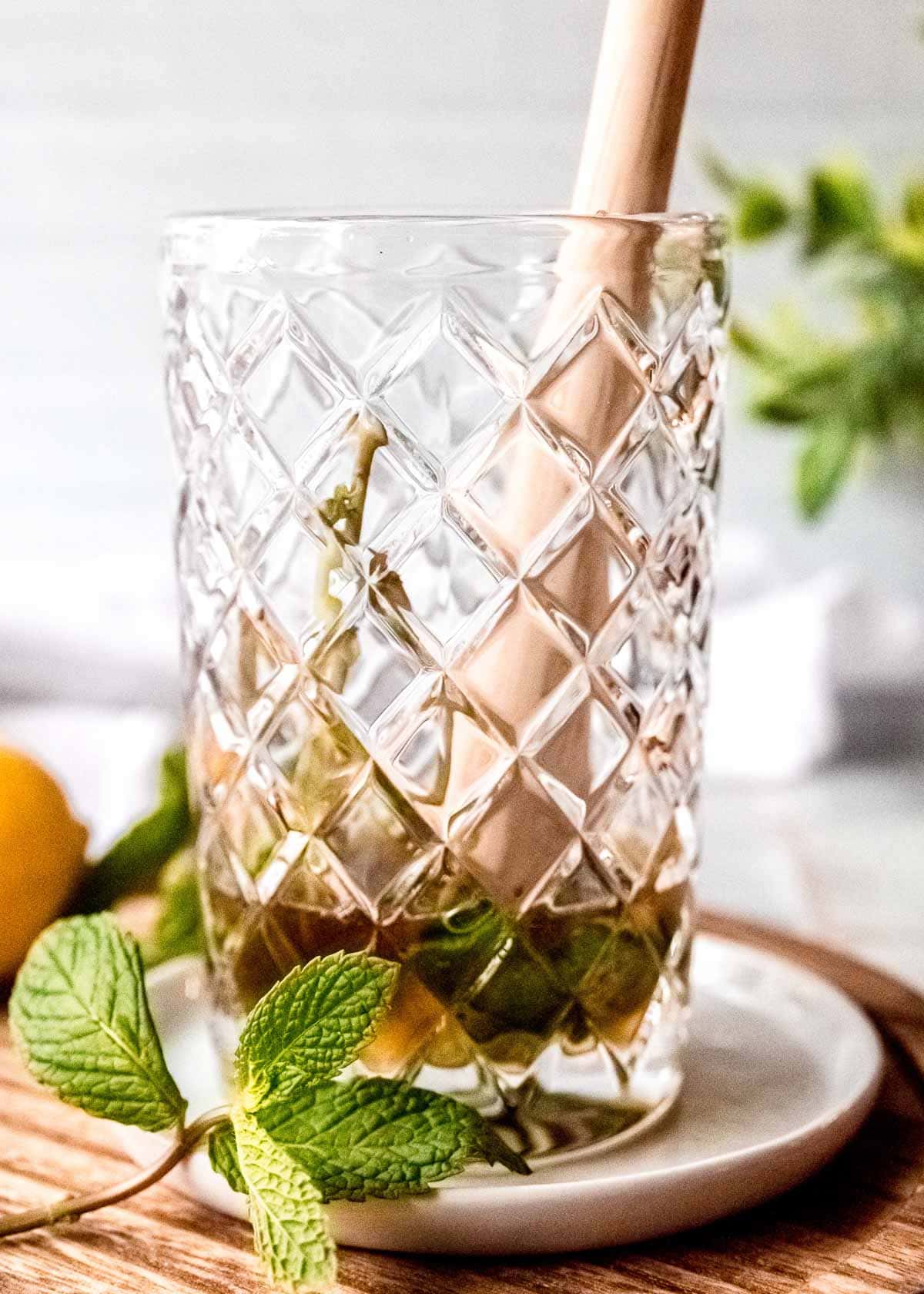 muddling mint and simple syrup in a clear glass