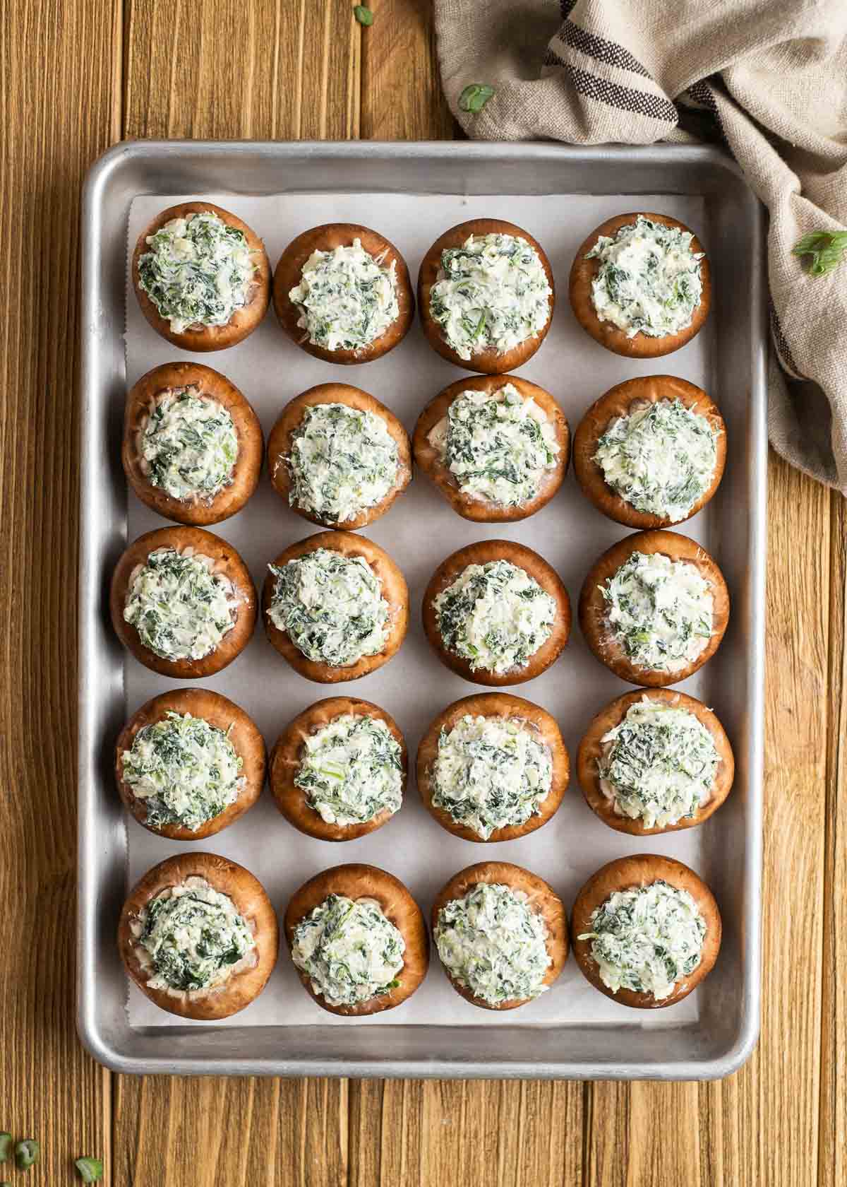 20 baby bella mushrooms stuffed with a spinach and cheese mixture on a lined baking pan