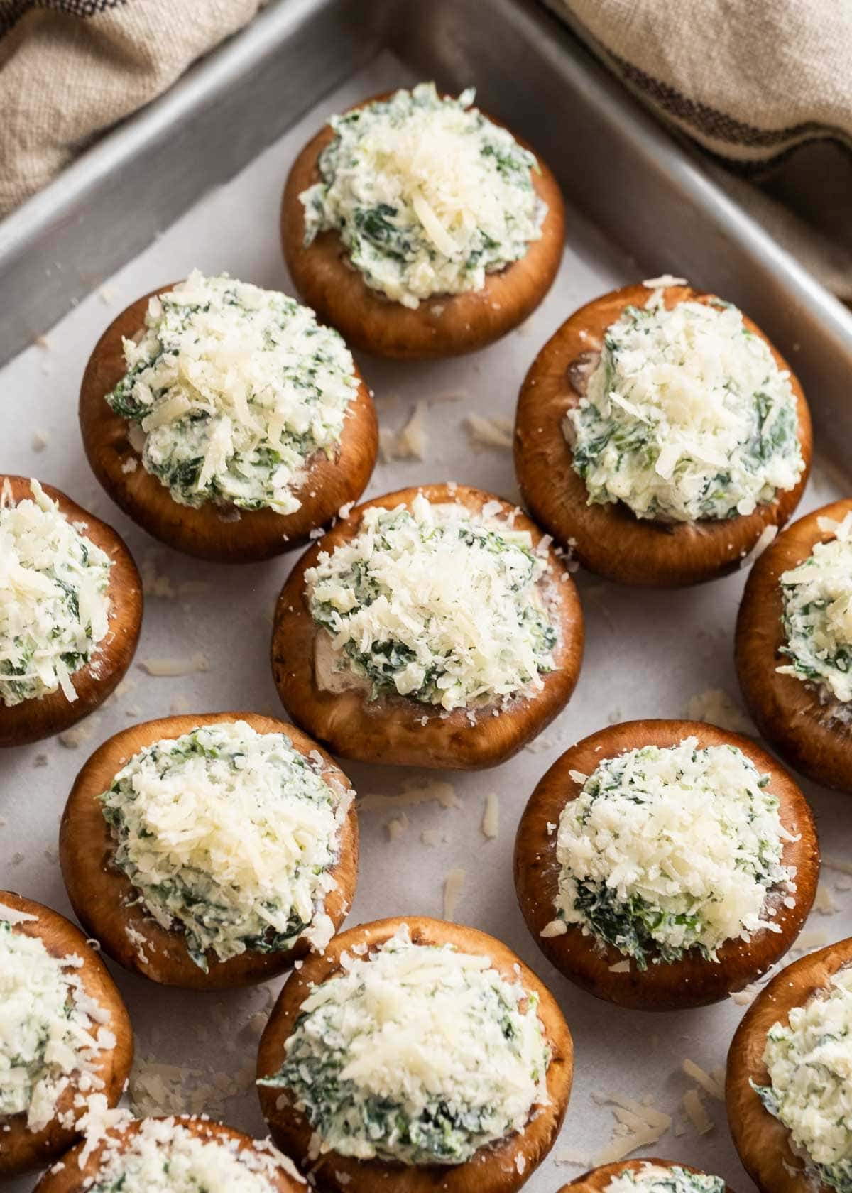 raw mushrooms stuffed with cheesy spinach mixture on a baking pan