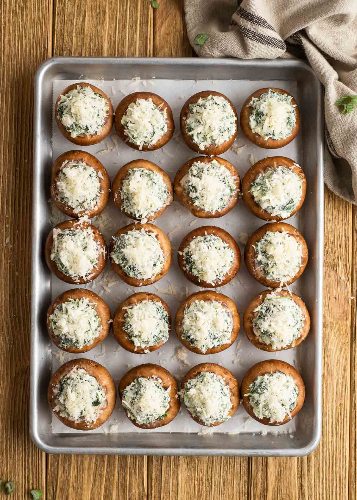 spinach stuffed mushrooms topped with parmesan cheese on a lined baking pan
