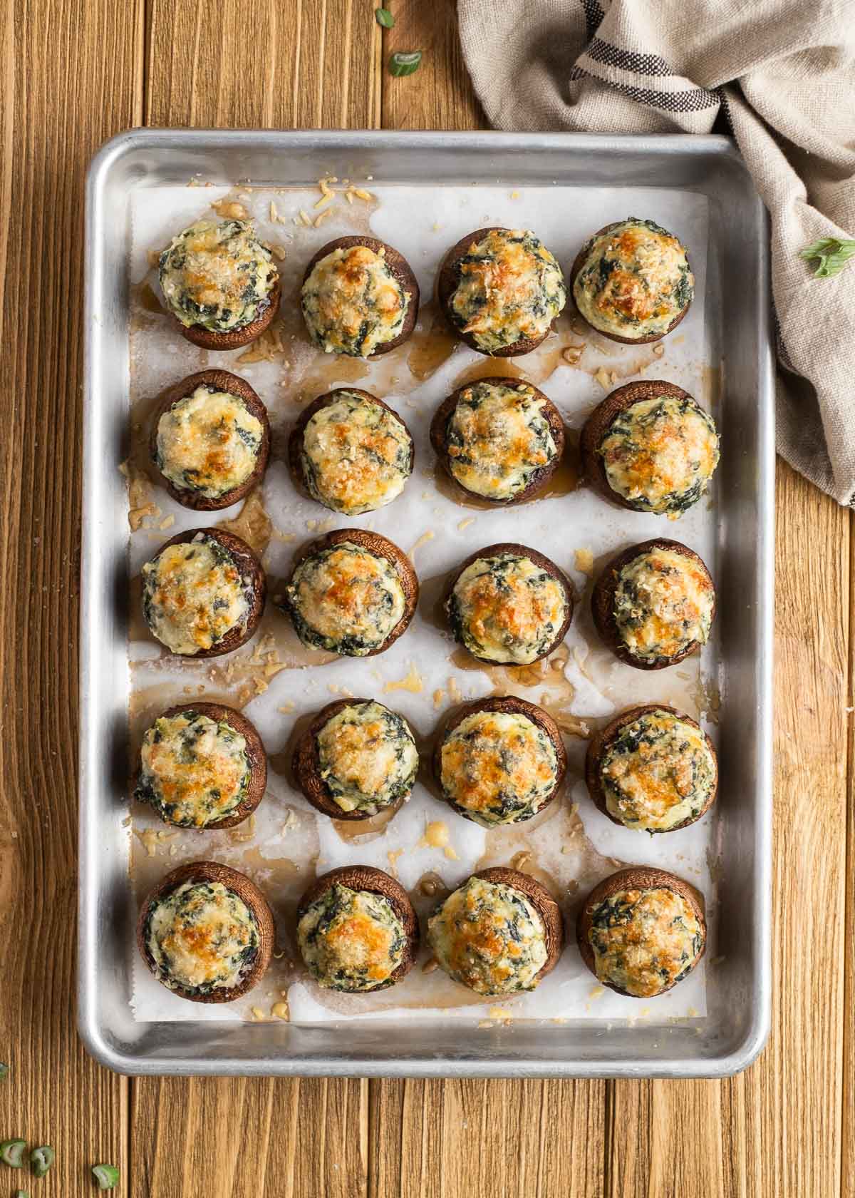 an overhead shot of all 20 spinach stuffed mushrooms baked on a parchment paper lined pan