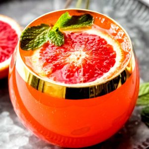 a close up shot of a blood orange cocktail recipe garnished with mint