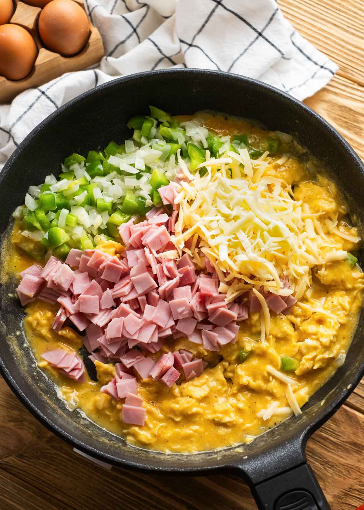 all loaded breakfast scramble ingredients being added to cast iron skillet