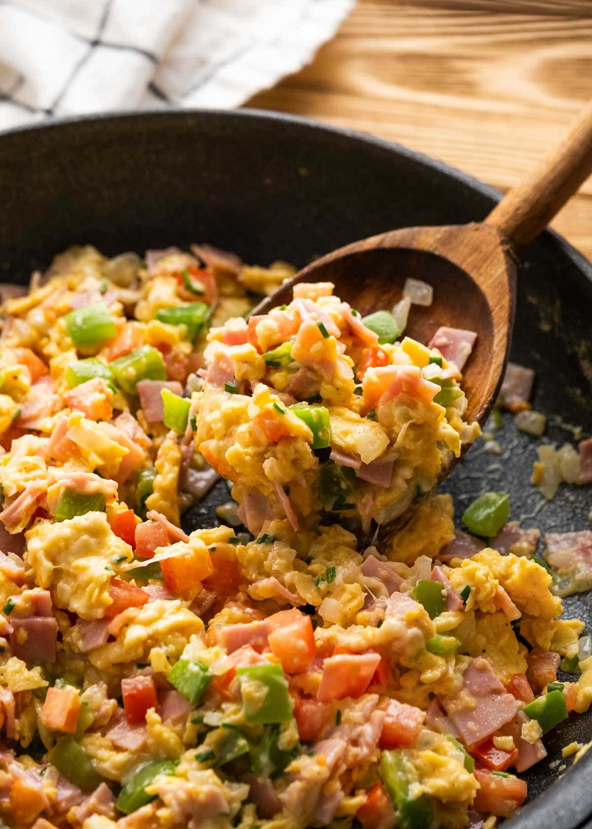scrambled eggs with ham and vegetables in a skillet with a wooden spoon