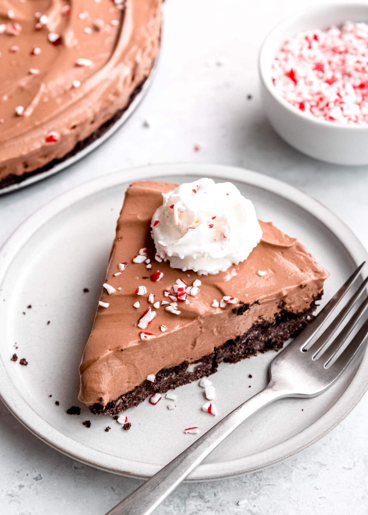 a slice of peppermint mocha pie on a plate topped with a dollop of whipped cream and some crushed candy canes