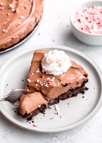 a fork slicing into a chilled no bake peppermint mocha pie topped with whipped cream and crushed peppermints