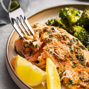 close up image of salmon and broccoli and a fork on a white plate