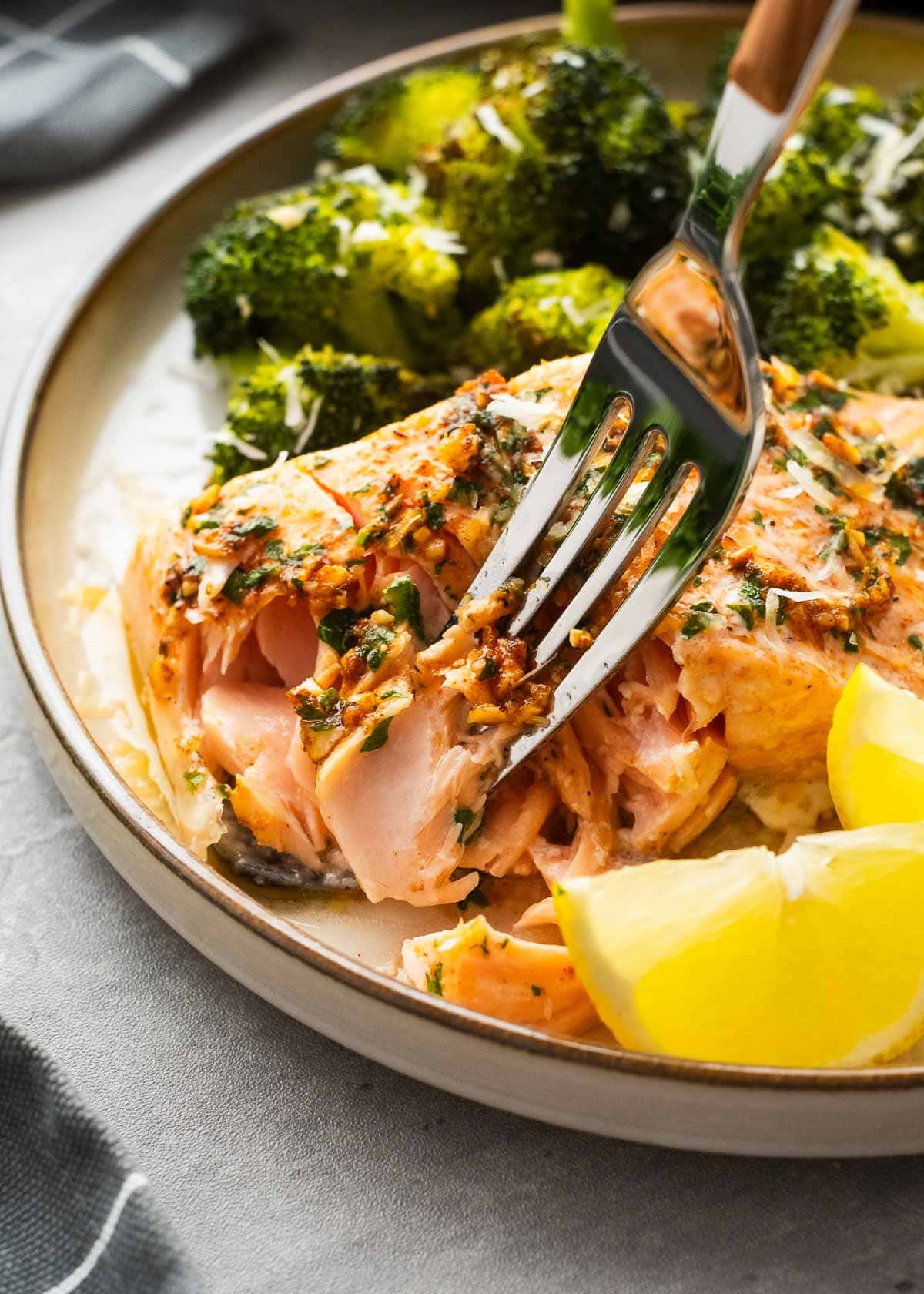 slice of salmon on a fork with salmon and broccol on a plate in the background