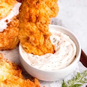 a crispy buttermilk fried chicken tender getting dunked into ranch dressing