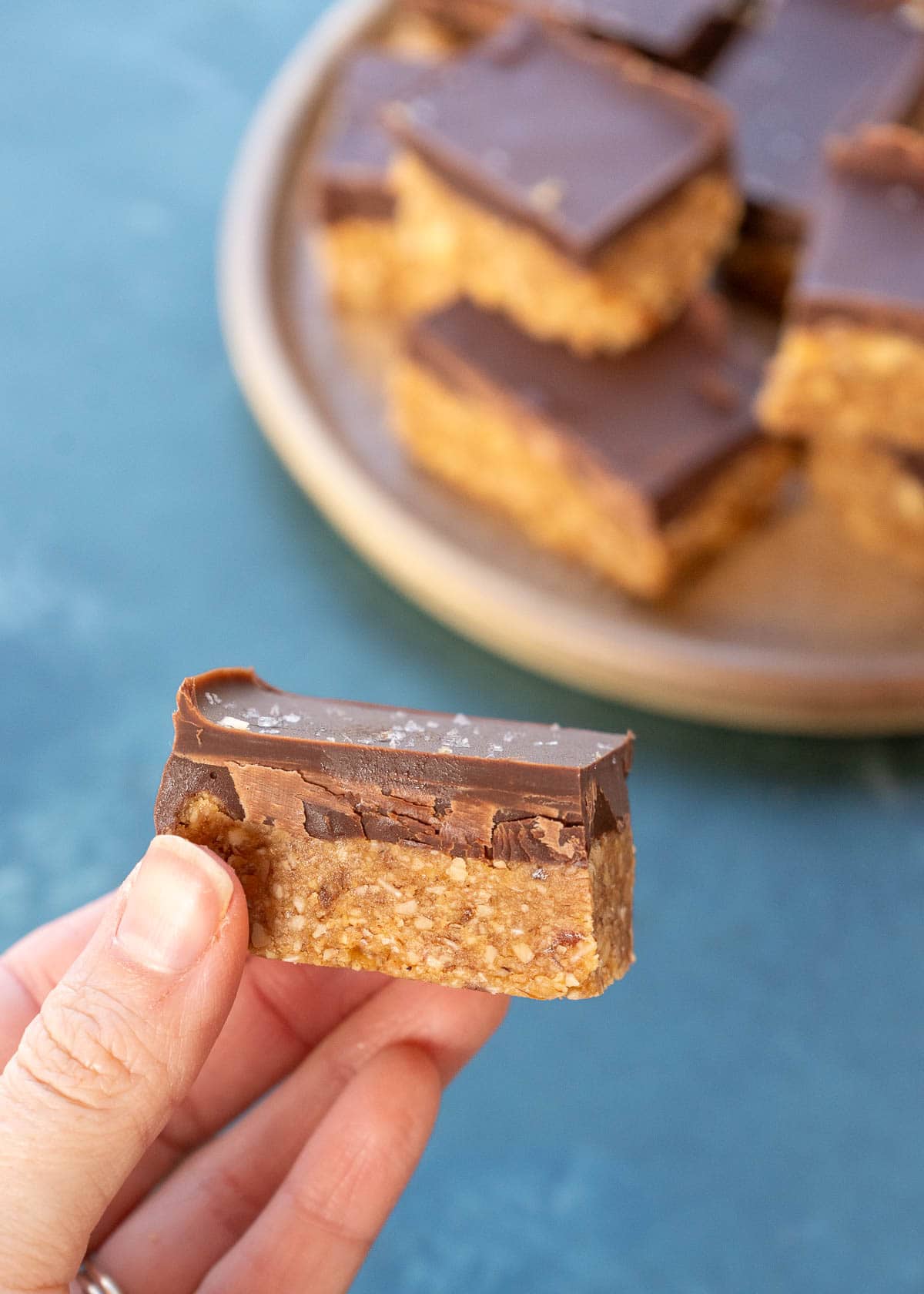 a hand holding a chocolate almond bar with a plate of no bake almond bars in the background