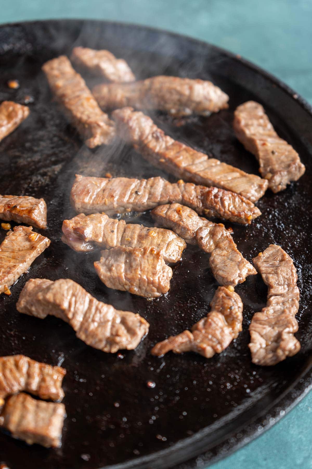 Strips of marinaded sirloin steak cooking on a skillet for an easy steak wrap