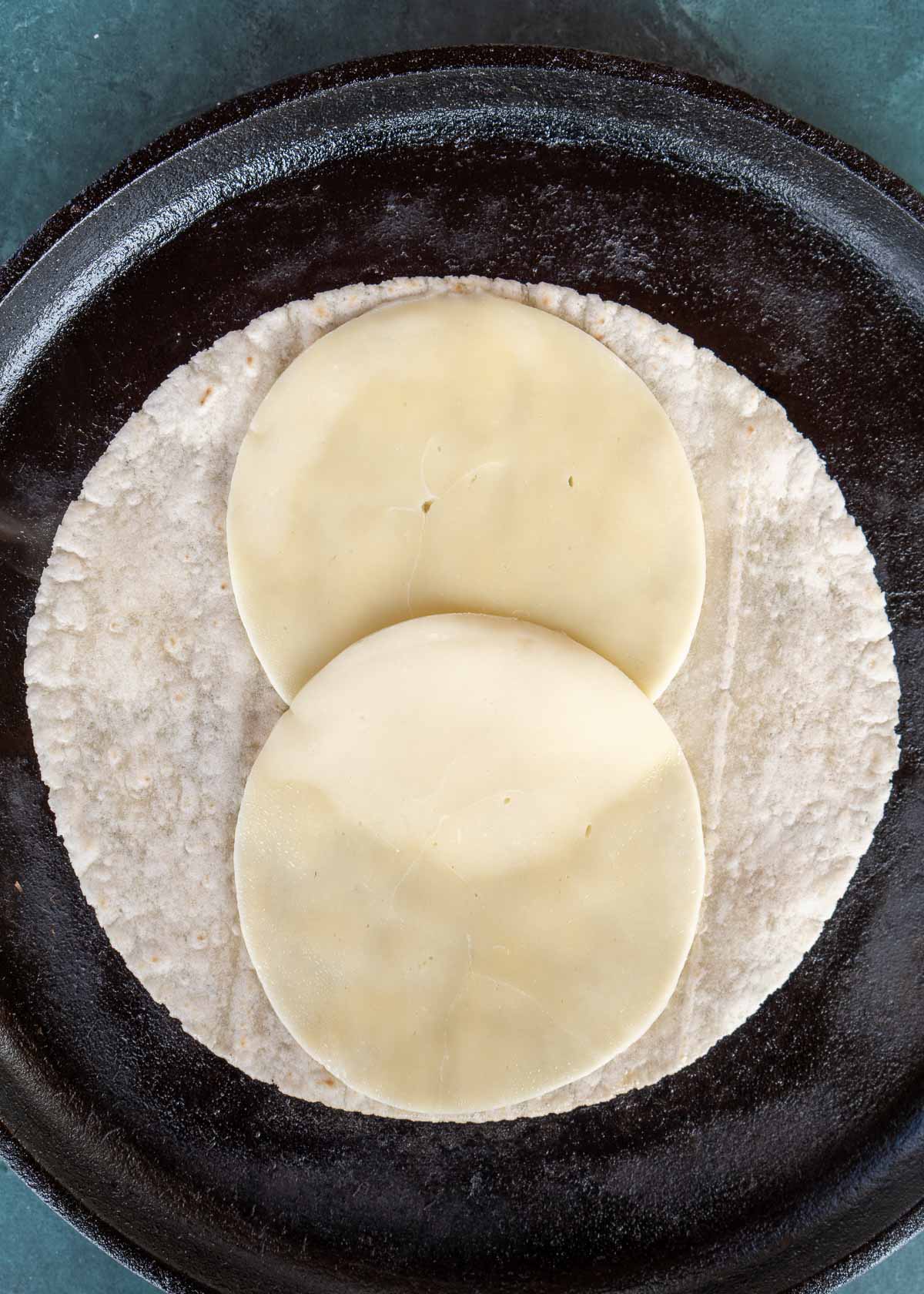a tortilla warming on a skillet with two slices of provolone for an easy steak wrap