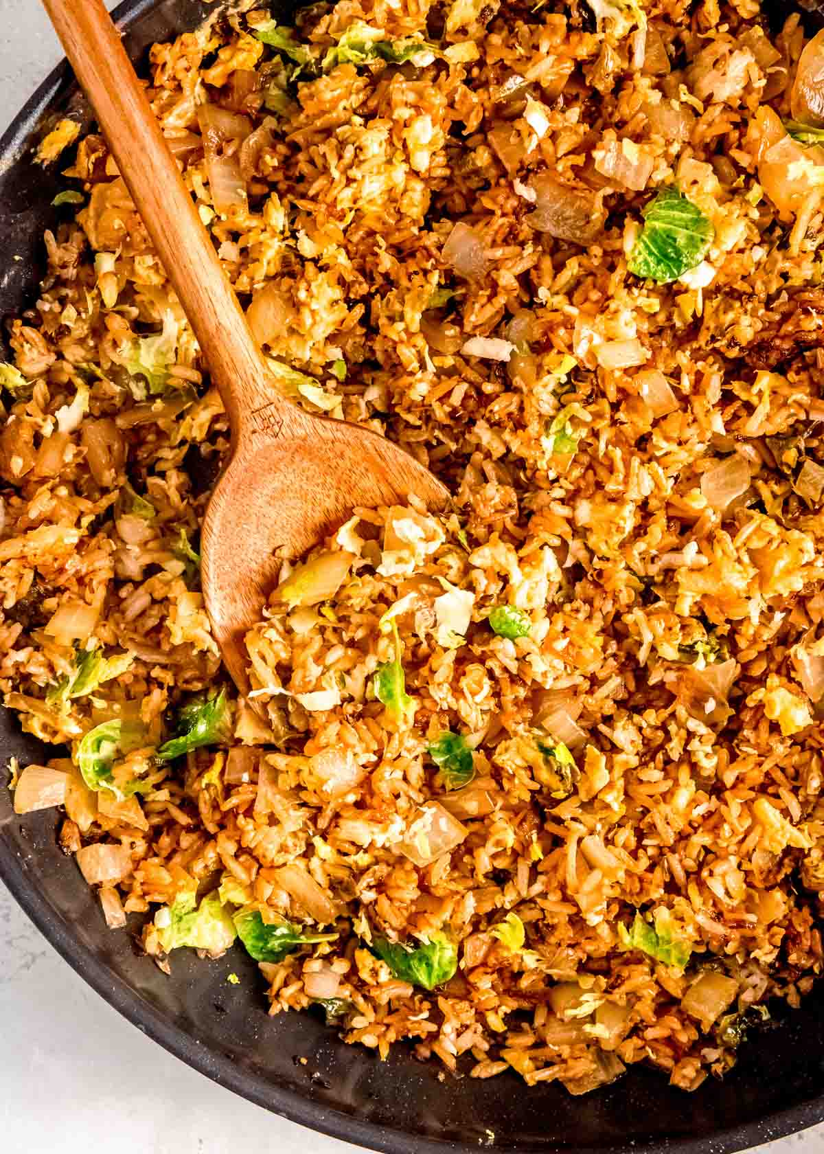 a large wooden spoon scooping up brussels sprout fried rice for a vegetarian side dish