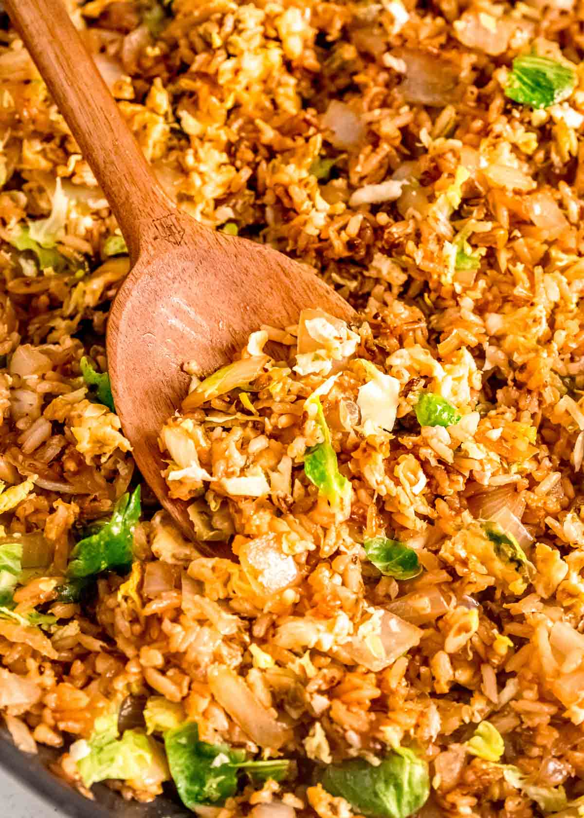 brussels sprout fried rice in a pan stirred with a wooden spoon